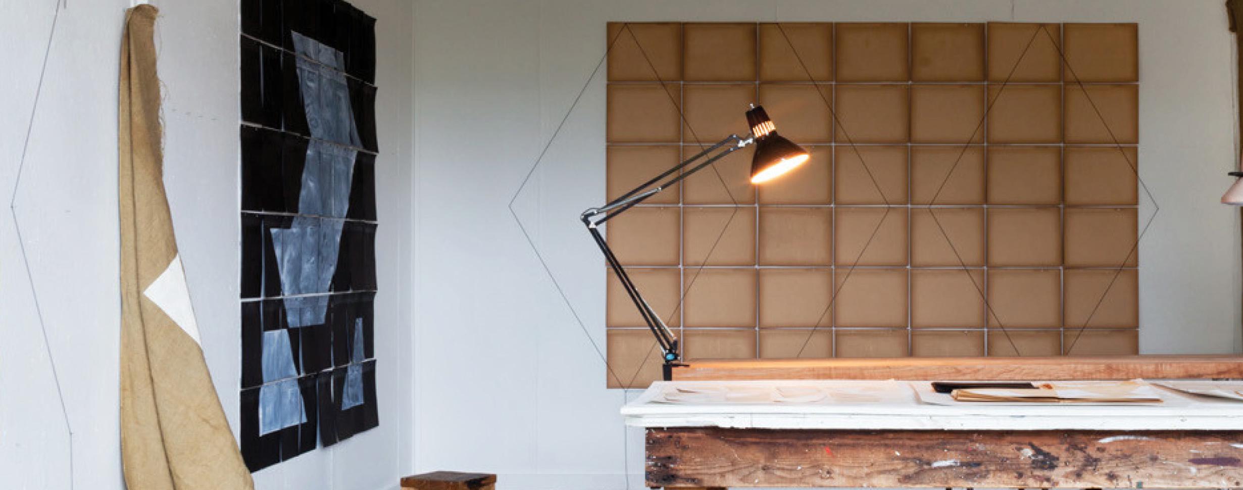 studio work table with clamped light; tan grid behind with thin lined diamond shapes laid on top