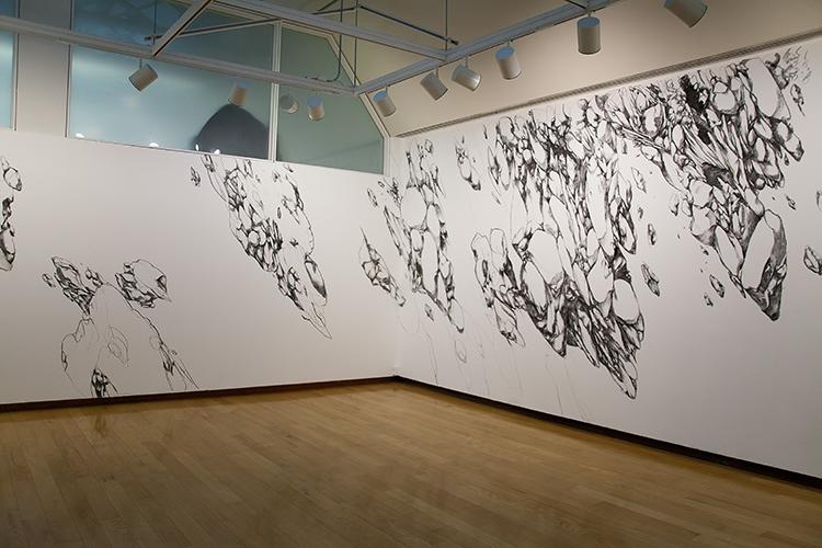 corner of a gallery with charcoal wall drawings of rocklike forms